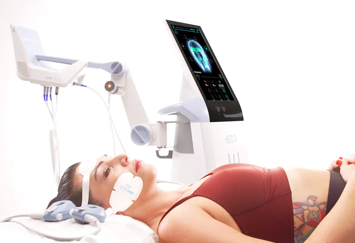 A female lying down using the EMFACE machine while it smooths and tightens her face.